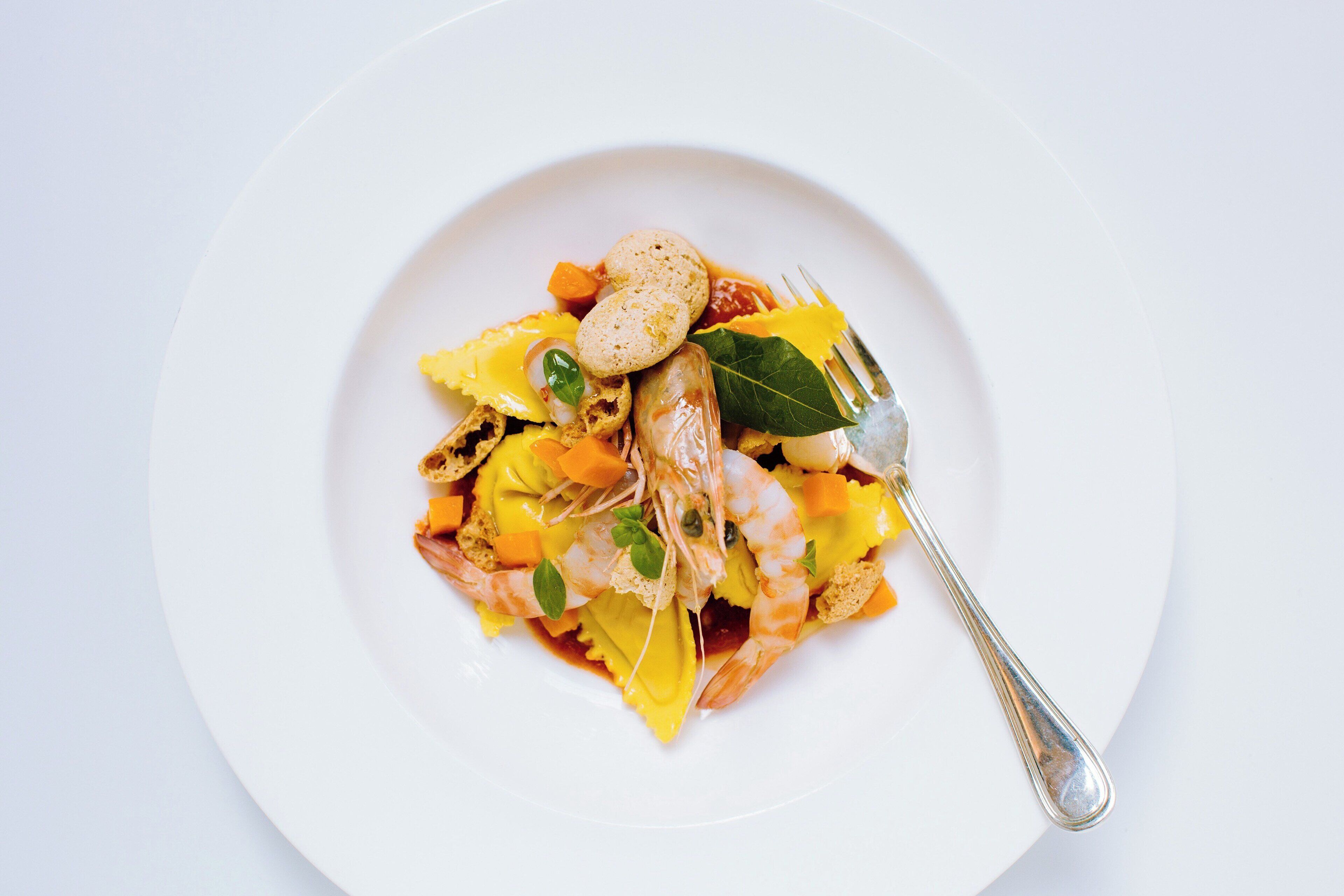 Ein weißer Teller mit einem Seafood-Gericht, darunter Garnelen, Gemüse und ein Lorbeerblatt als Garnitur.