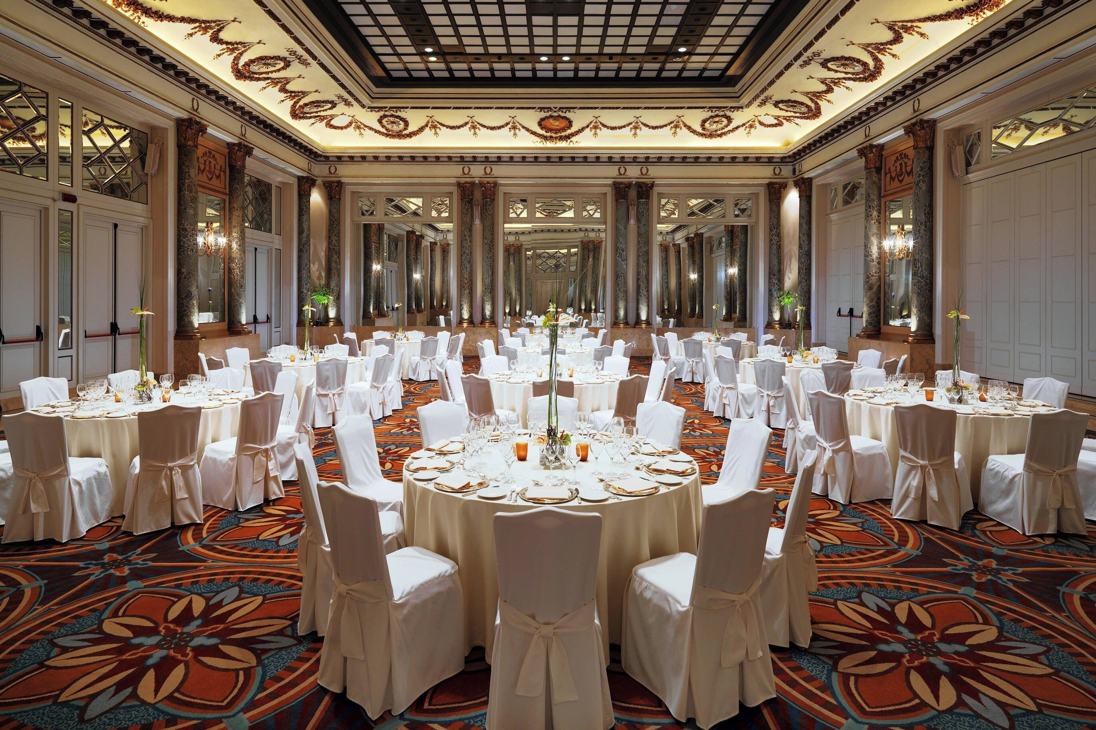 A banquet hall with round tables, white chairs, and a patterned carpet.