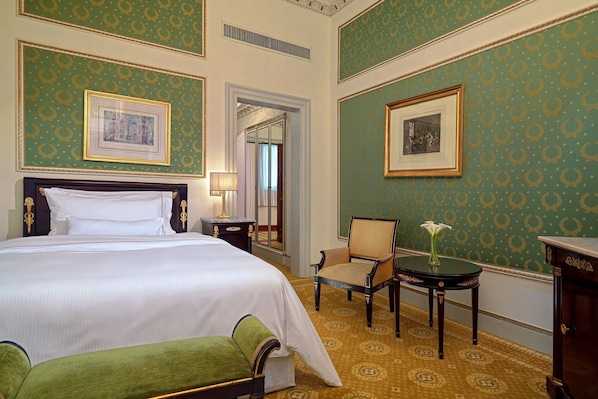 Habitación de hotel con una cama grande, una silla, una mesita con un florero y dos cuadros en las paredes.