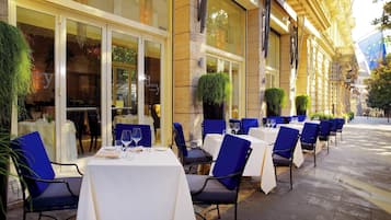 An outdoor dining area with tables and chairs, a building facade with large windows, and a street view.
