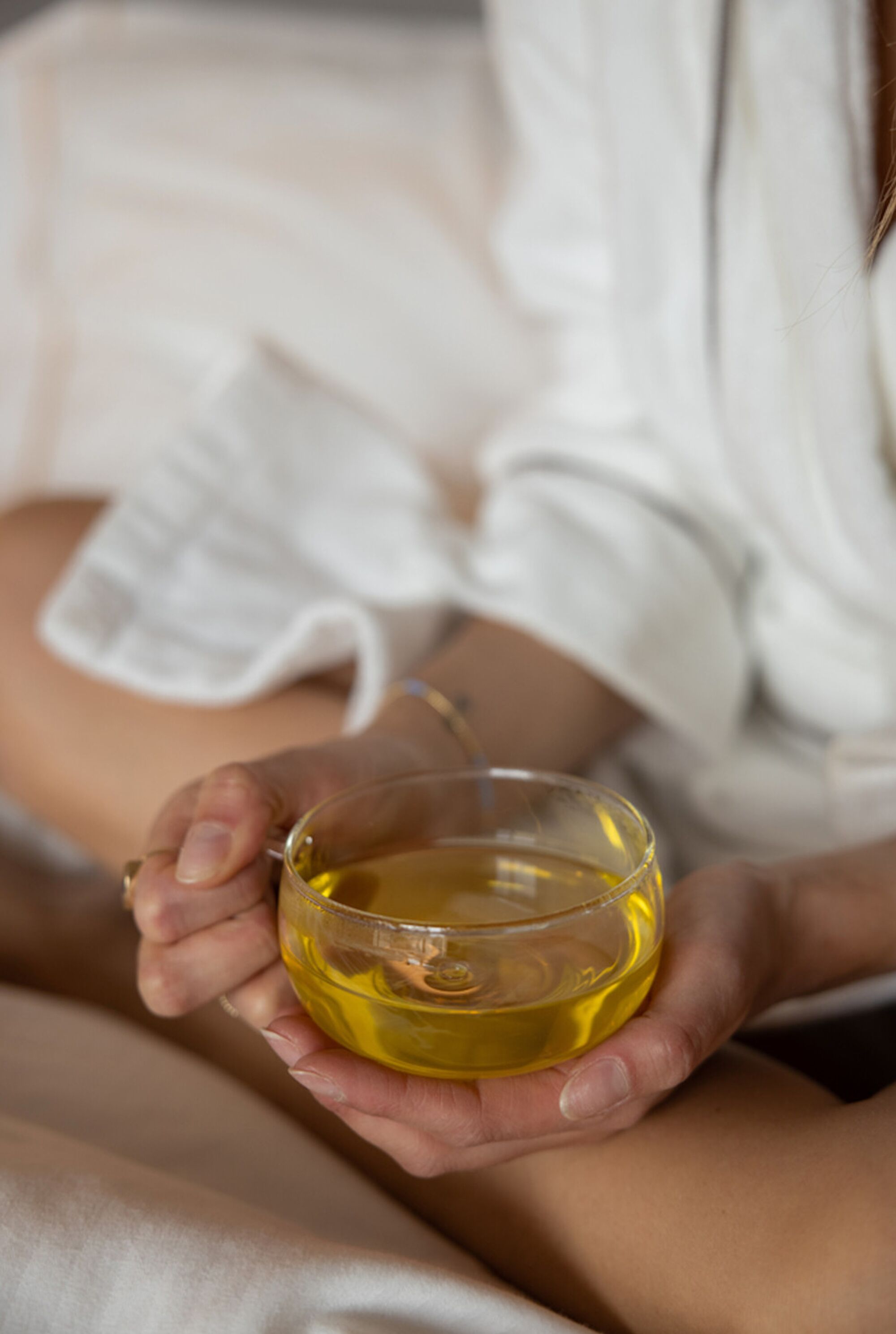Una persona sosteniendo un pequeño recipiente de vidrio con líquido amarillo, probablemente aceite o loción, en un ambiente tranquilo.