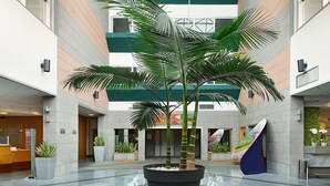 A spacious atrium with a high ceiling, large potted plants, and a central staircase.