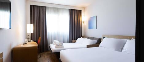 A hotel room with two beds, a desk, a chair, a TV, and a window with curtains.