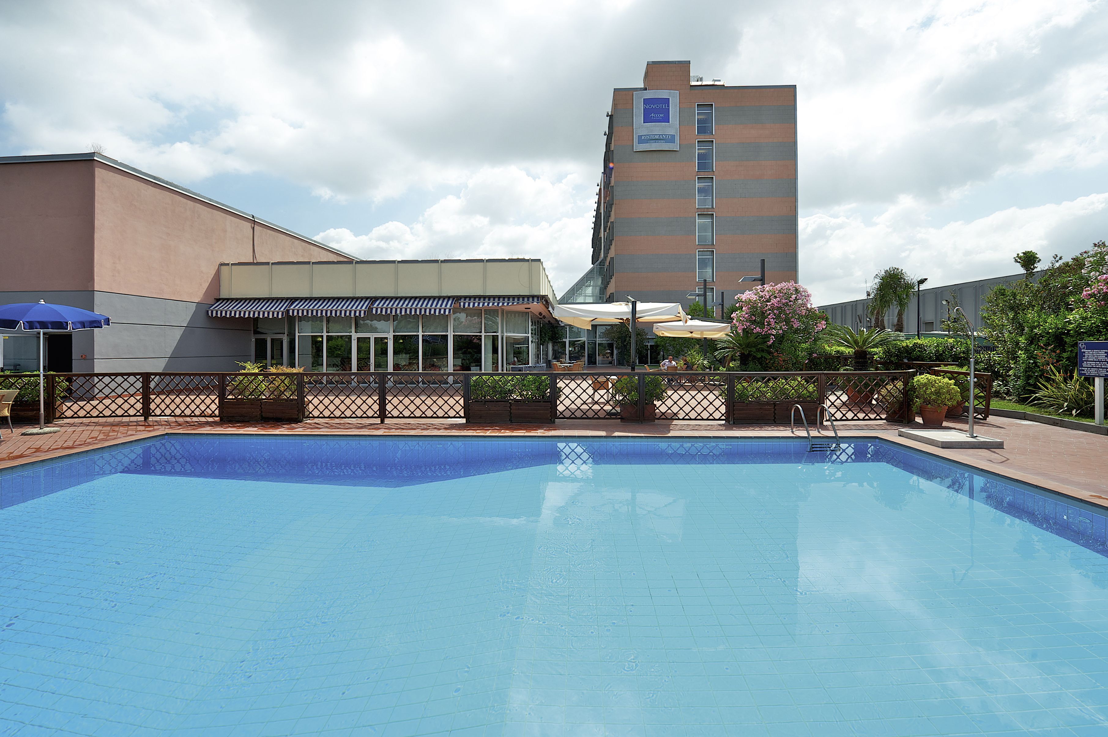 A swimming pool with a fenced area, a building with a sign that reads "Marriott", and a clear sky.