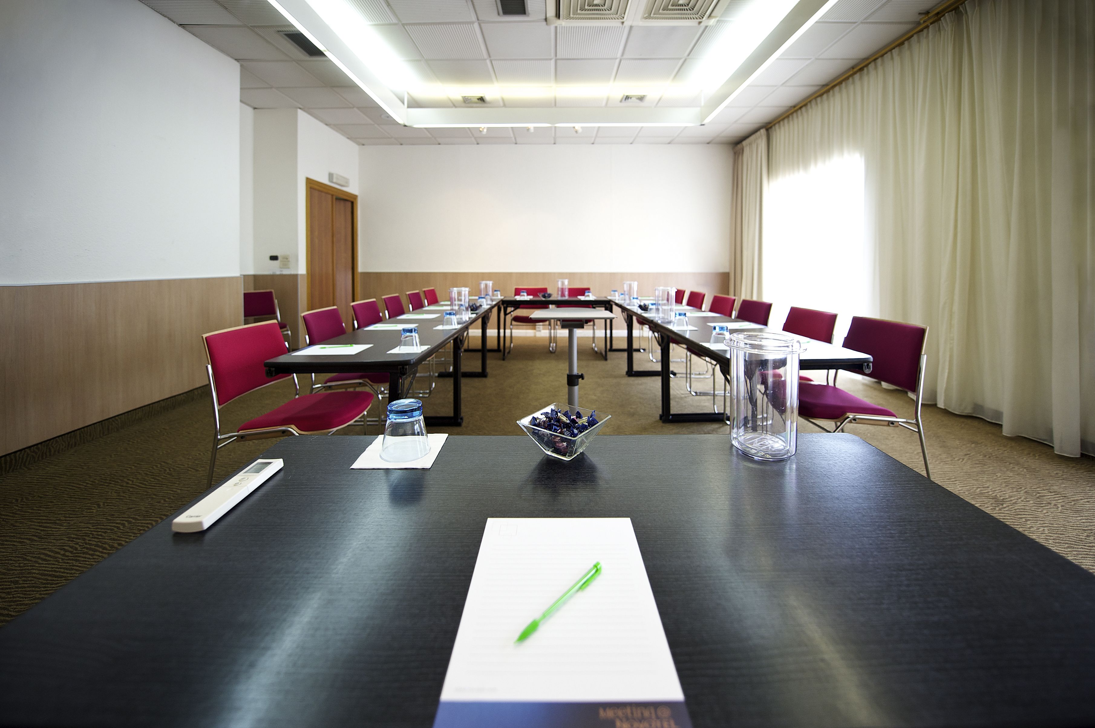 Una sala de conferencias con una larga mesa, sillas rojas y una pizarra.