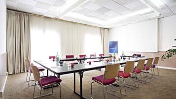 Une salle de conférence avec une longue table, des chaises rouges, un écran de projection et une grande fenêtre avec des rideaux.