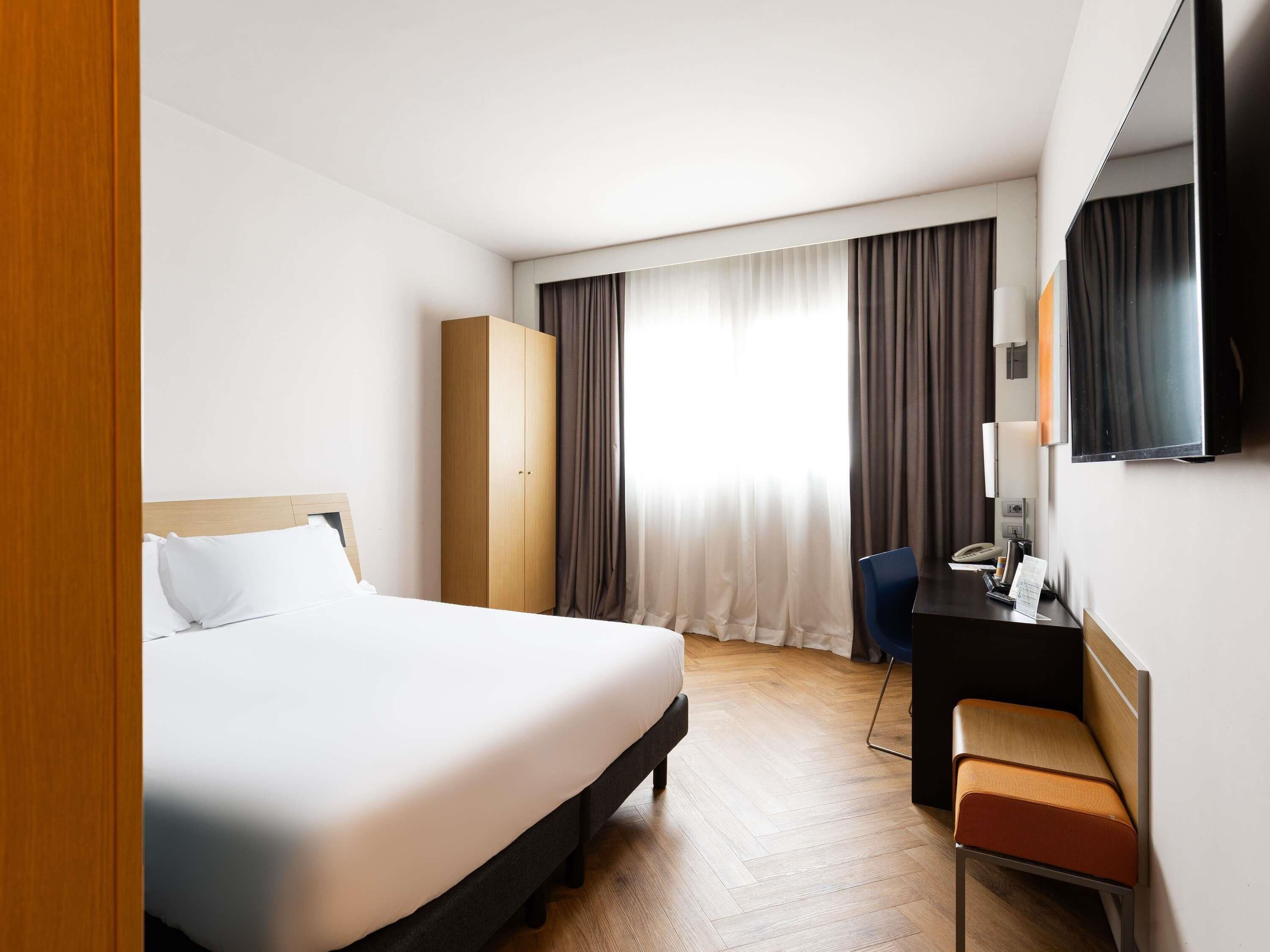 A hotel room with a bed, a desk, a chair, and a wardrobe.