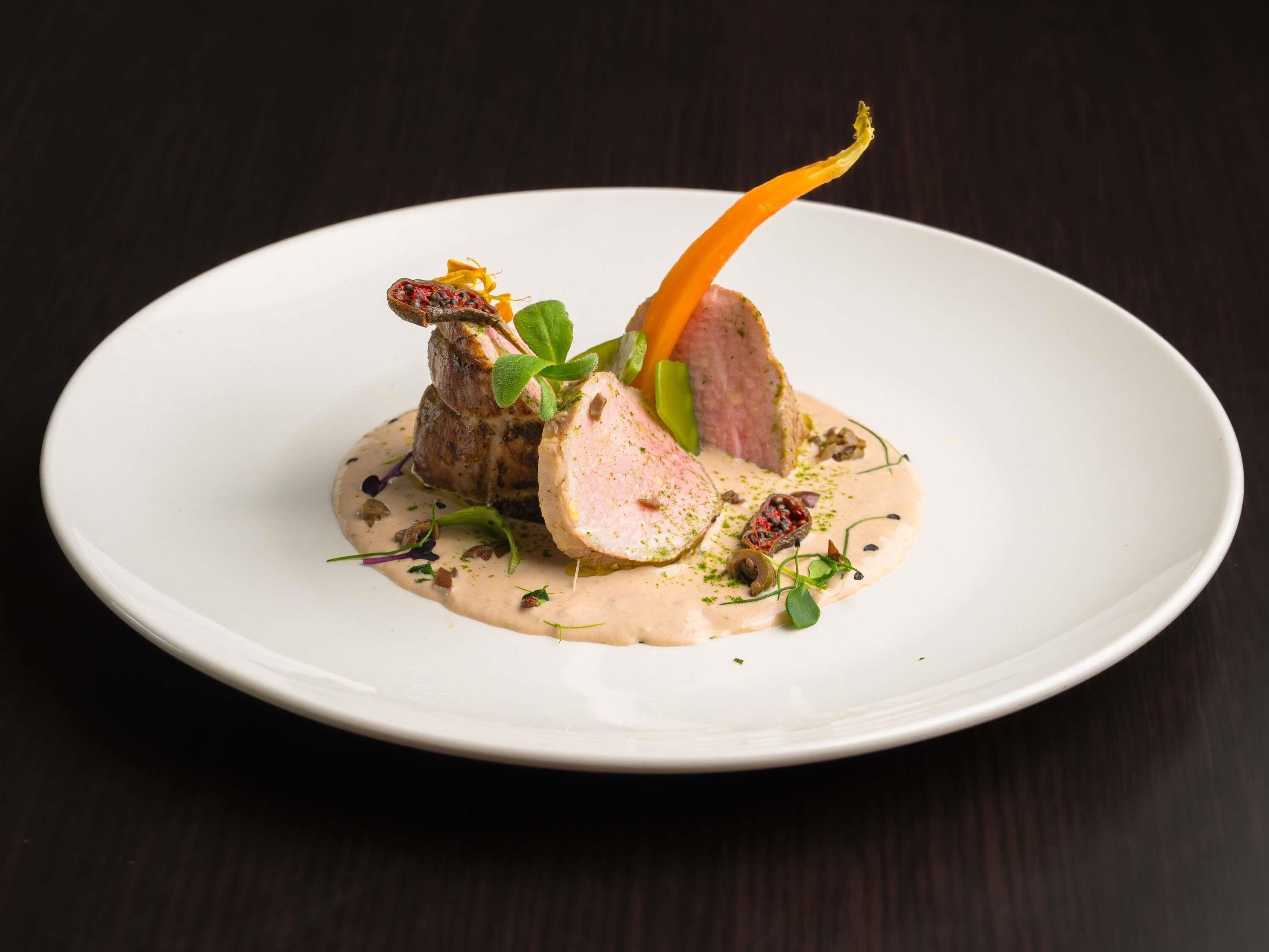 A white plate with a dish of sliced meat, vegetables, and sauce.