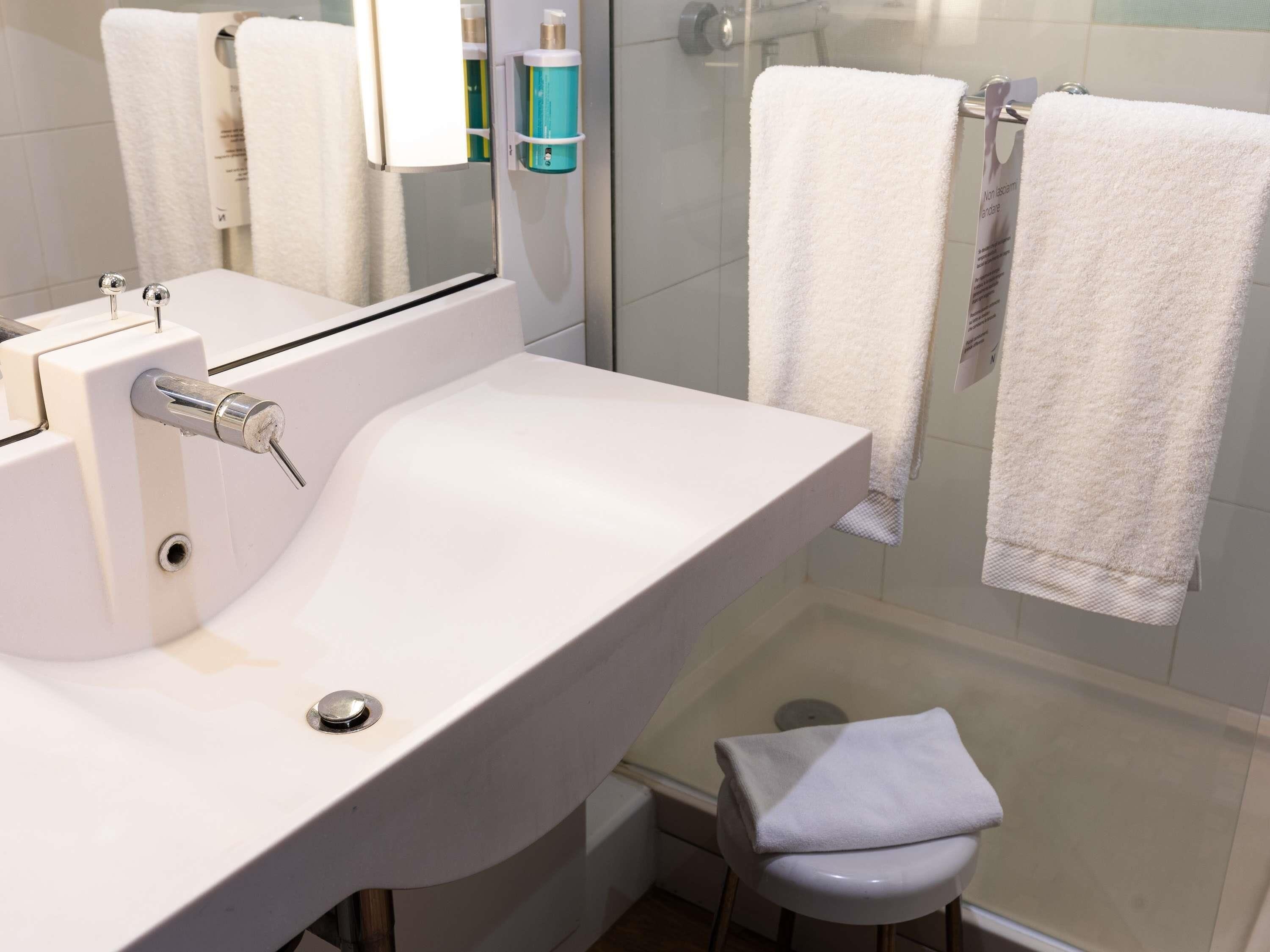Une salle de bain avec un lavabo blanc, un miroir, une cabine de douche en verre et deux serviettes suspendues à un porte-serviettes.