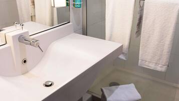 A bathroom with a white sink, a mirror, a glass shower enclosure, and two towels hanging on a rack.
