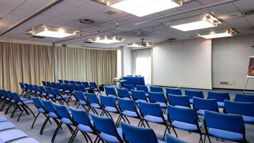 Ein Konferenzraum mit Reihen blauer Stühle, einer Projektionsleinwand und Deckenleuchten.