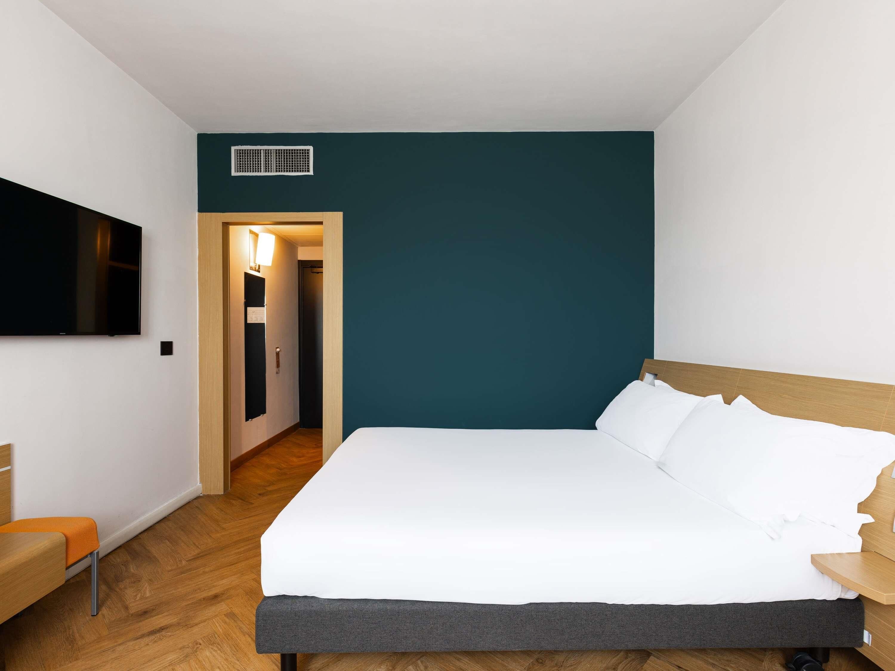 Et moderne hotelværelse med en stor seng, et fladskærms-TV og en træbænk.