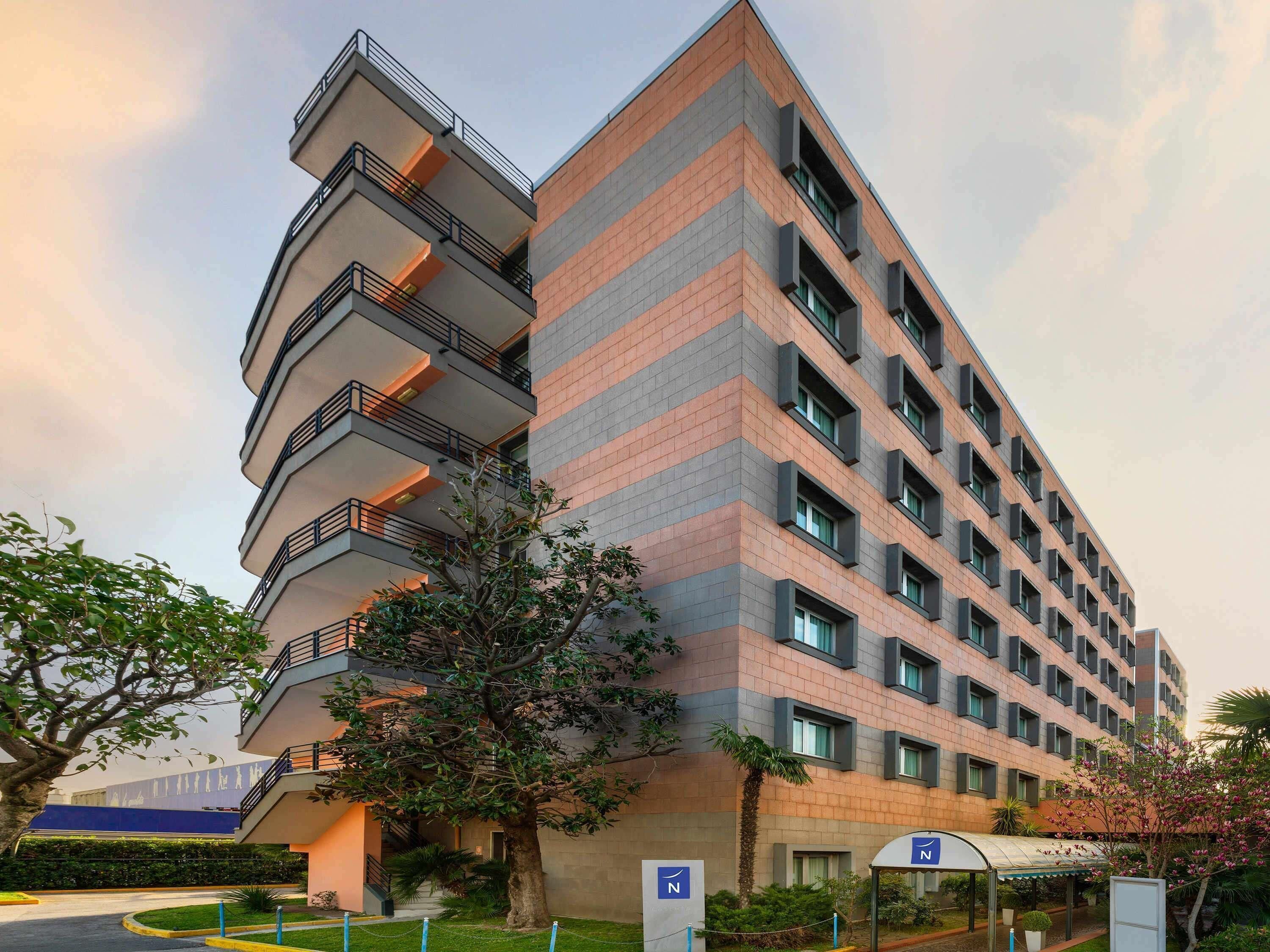 Un hôtel à plusieurs étages doté de balcons, d’un espace extérieur couvert et d’un panneau indiquant l’emplacement du parking.