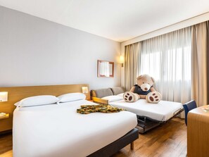 Hotellihuone, jossa on kaksi sänkyä, sohva, pehmolelu ja ikkuna, jossa on verhot.