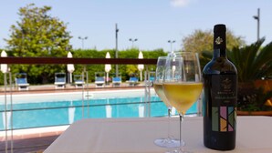 A bottle of wine and two glasses on a table with a view of a swimming pool and lounge chairs.