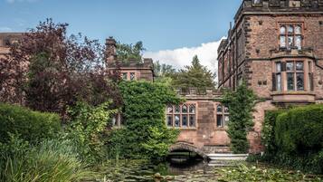 A historic building with a pond, surrounded by lush greenery and a bridge.