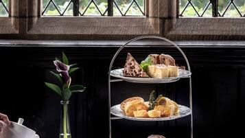 A tiered dessert stand with pastries and scones, a vase with a flower, and a table with cups and saucers.