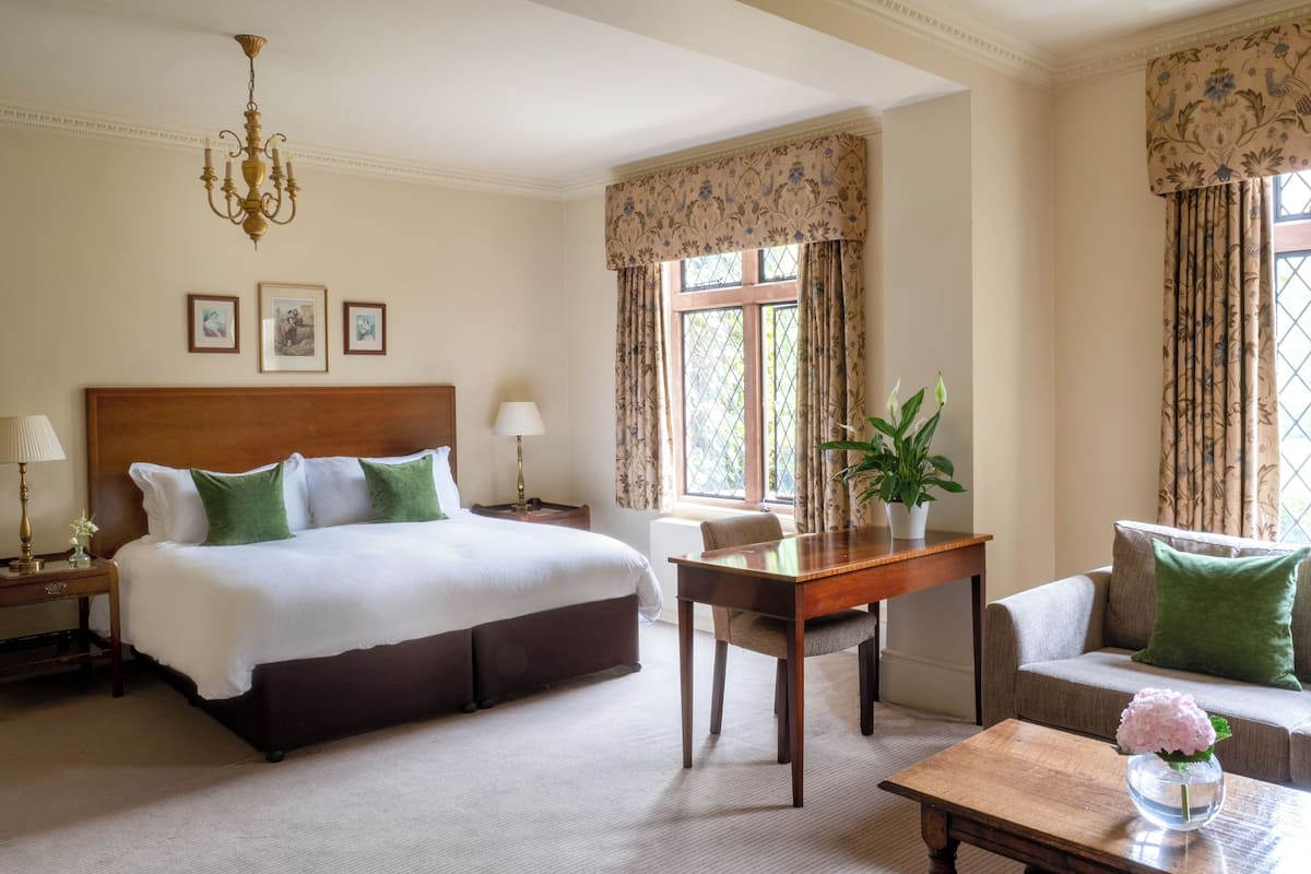 A hotel room with a large bed, a wooden nightstand, a table, a sofa, and a chandelier.