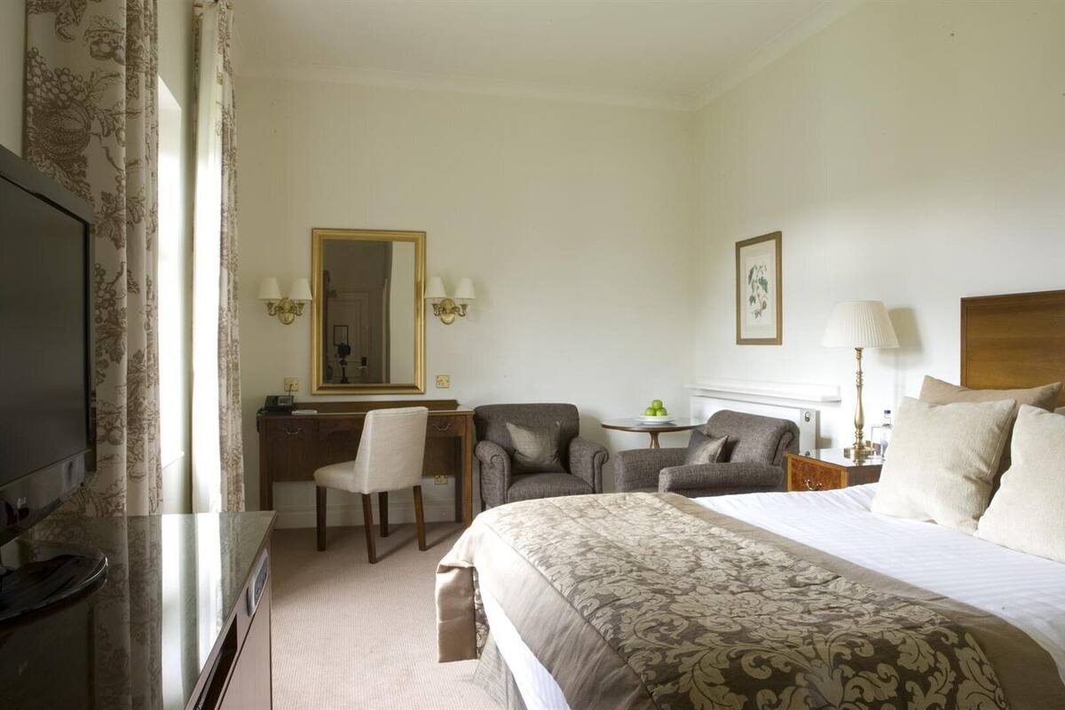 A hotel room with a bed, a desk, a chair, a television, and a mirror.