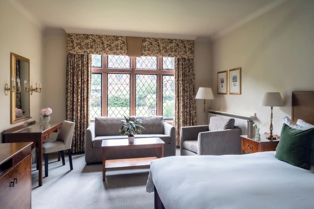 A hotel room with a bed, two armchairs, a sofa, a small table, a desk, and a window with curtains.
