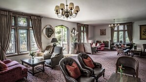 A spacious room with a patterned carpet, leather armchairs, a wooden coffee table, and a chandelier. - New Hall Hotel & Spa (Sutton Coldfield)