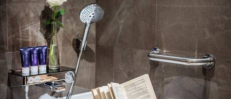 A bathtub with a showerhead, a wooden tray with a book and a mug, and toiletries on a shelf.