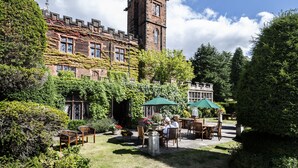 A historic building with ivy-covered walls and a tower, featuring outdoor seating with umbrellas. - New Hall Hotel & Spa (Sutton Coldfield)