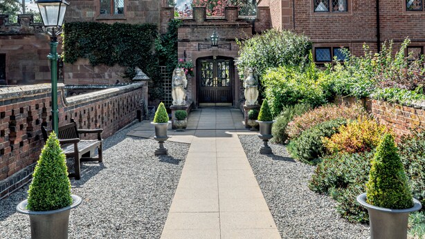 A courtyard with a paved walkway, stone lamp posts, and a brick building with a gate. - New Hall Hotel & Spa (Sutton Coldfield)