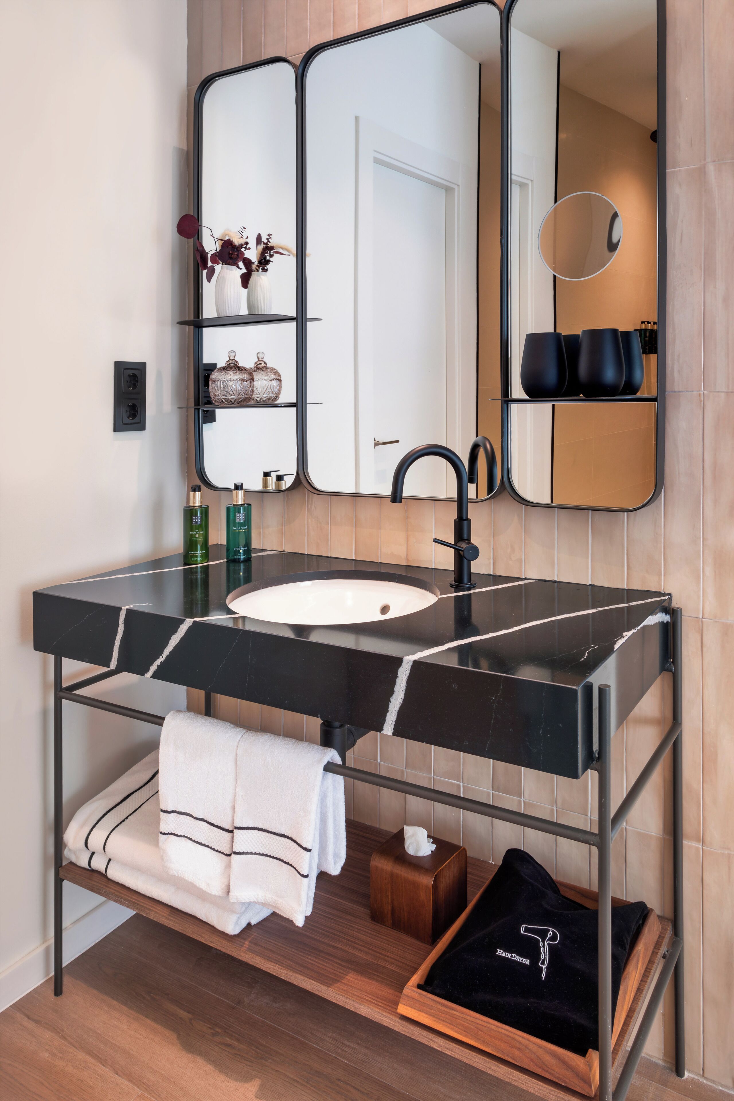 A modern bathroom with a black marble sink, a large mirror, and a towel rack.