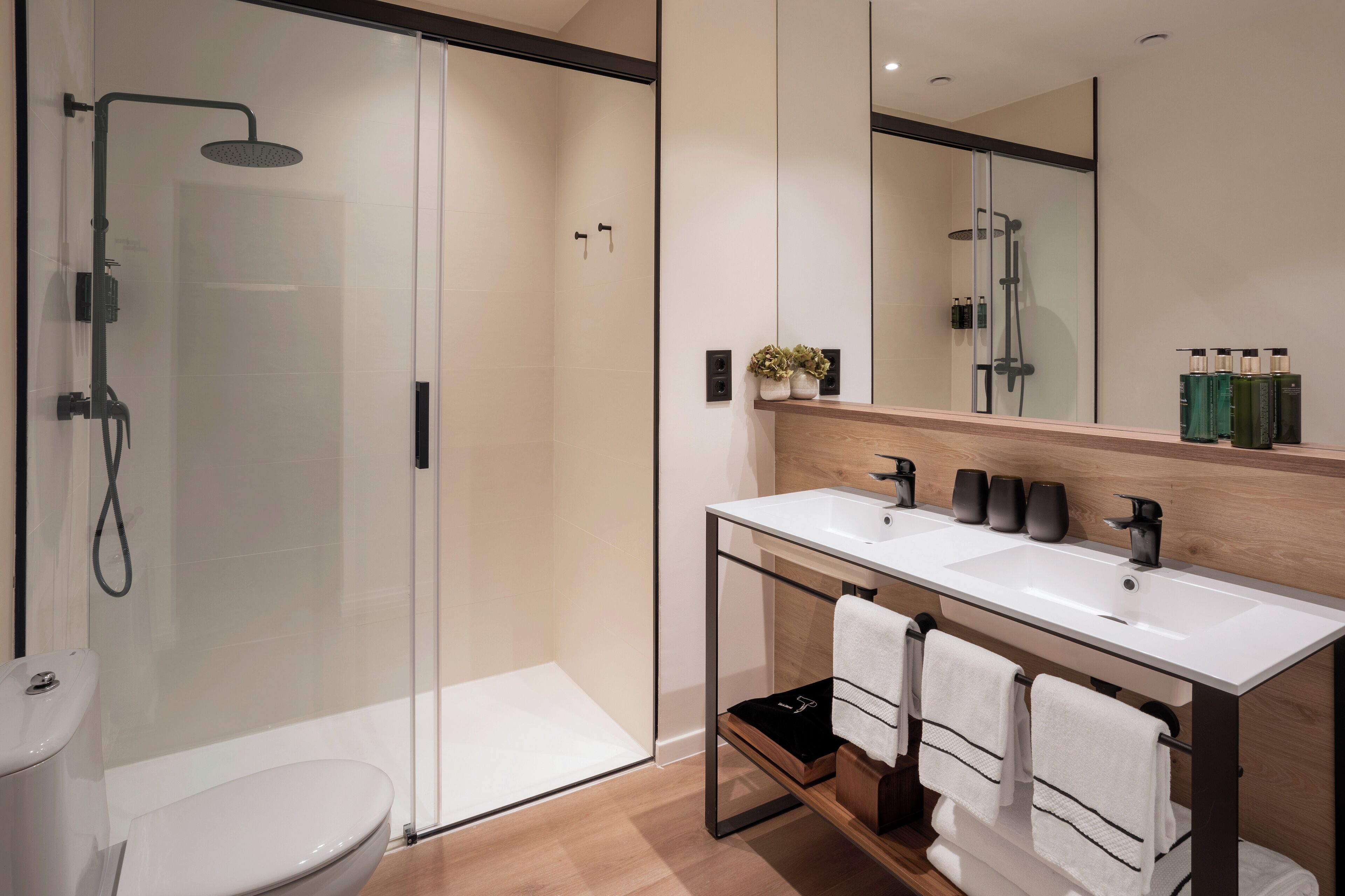 A modern bathroom with a glass shower enclosure, a white sink with a wooden countertop, and a large mirror above the sink.