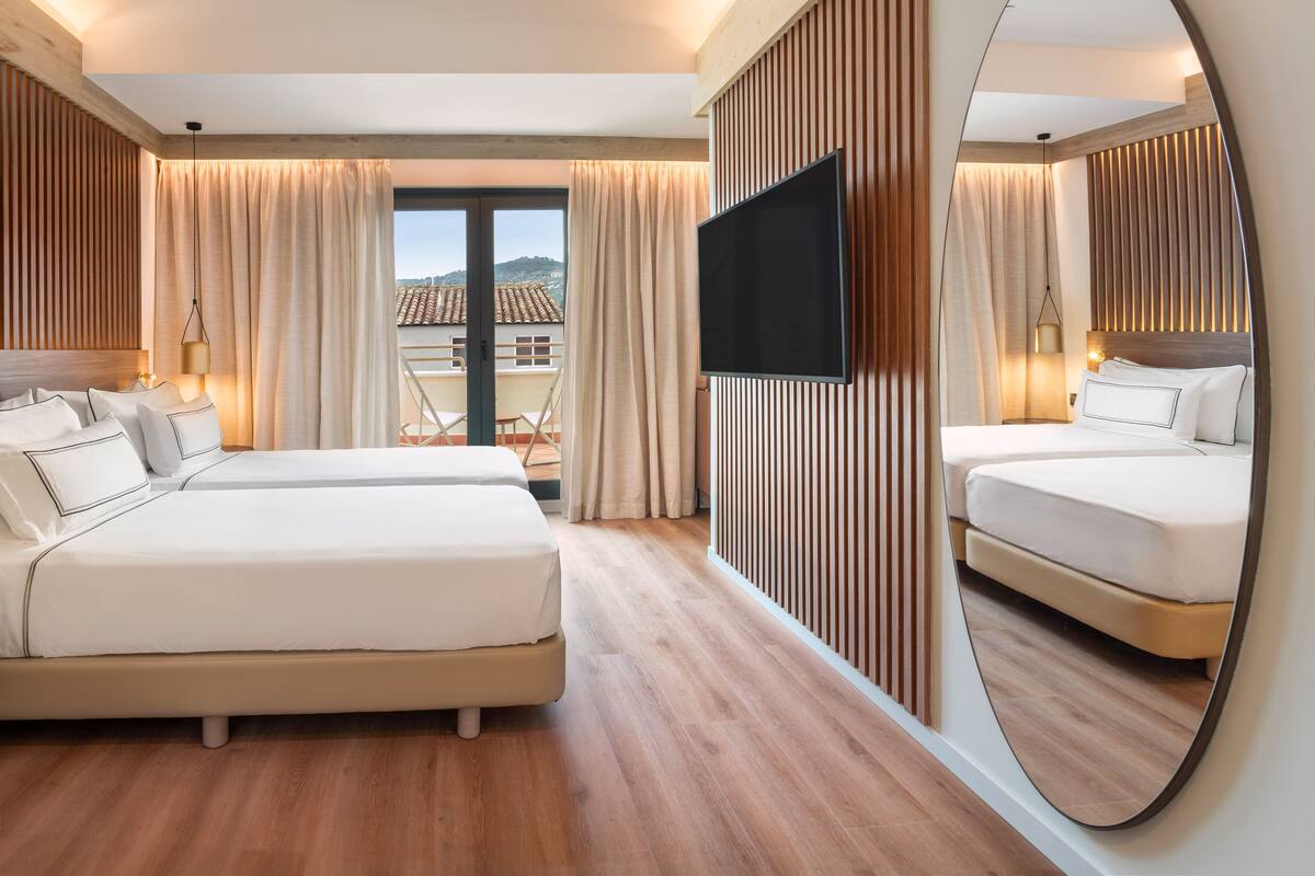 Habitación de hotel con dos camas, un televisor y un espejo grande.