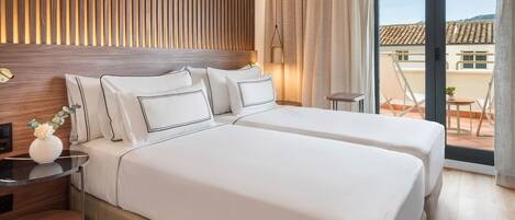 A hotel room with two beds, a wooden headboard, a nightstand with a lamp, and a view of the outside balcony.