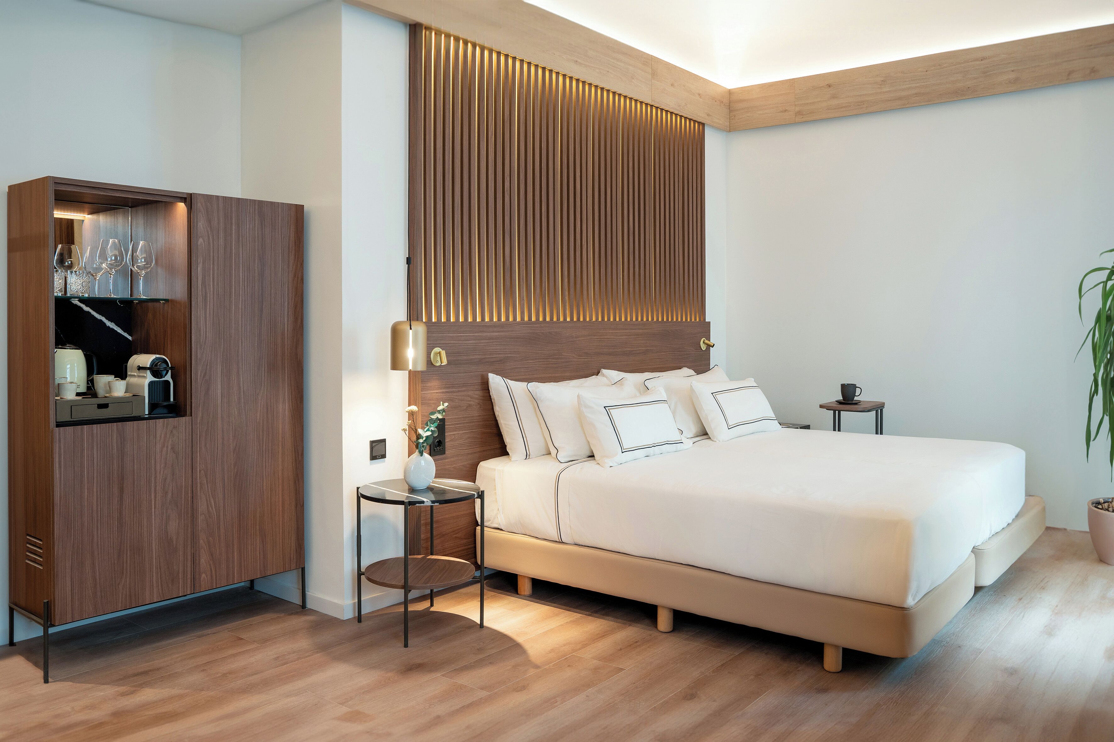A modern bedroom with a large bed, bedside tables, a wardrobe, and a potted plant.