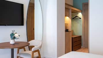 A bedroom with a bed, a chair, a table, a TV, a mirror, and a wardrobe.