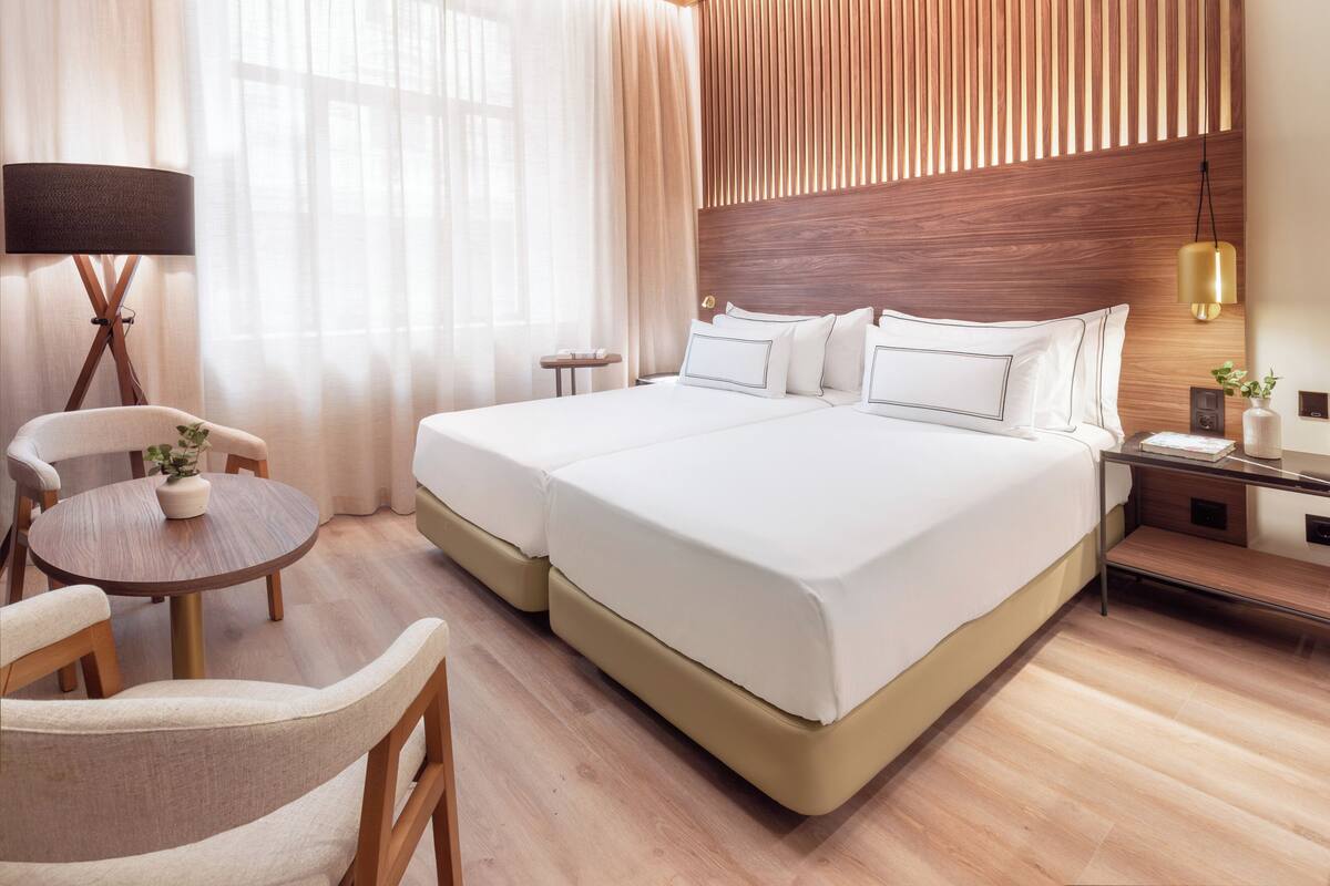 Una habitación de hotel con dos camas, un escritorio, una silla, una lámpara y una mesita de noche con una planta.