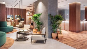 A modern reception area with a wooden reception desk, a seating area with a sofa and chairs, and potted plants. - Melia Granada Hotel (Granada)