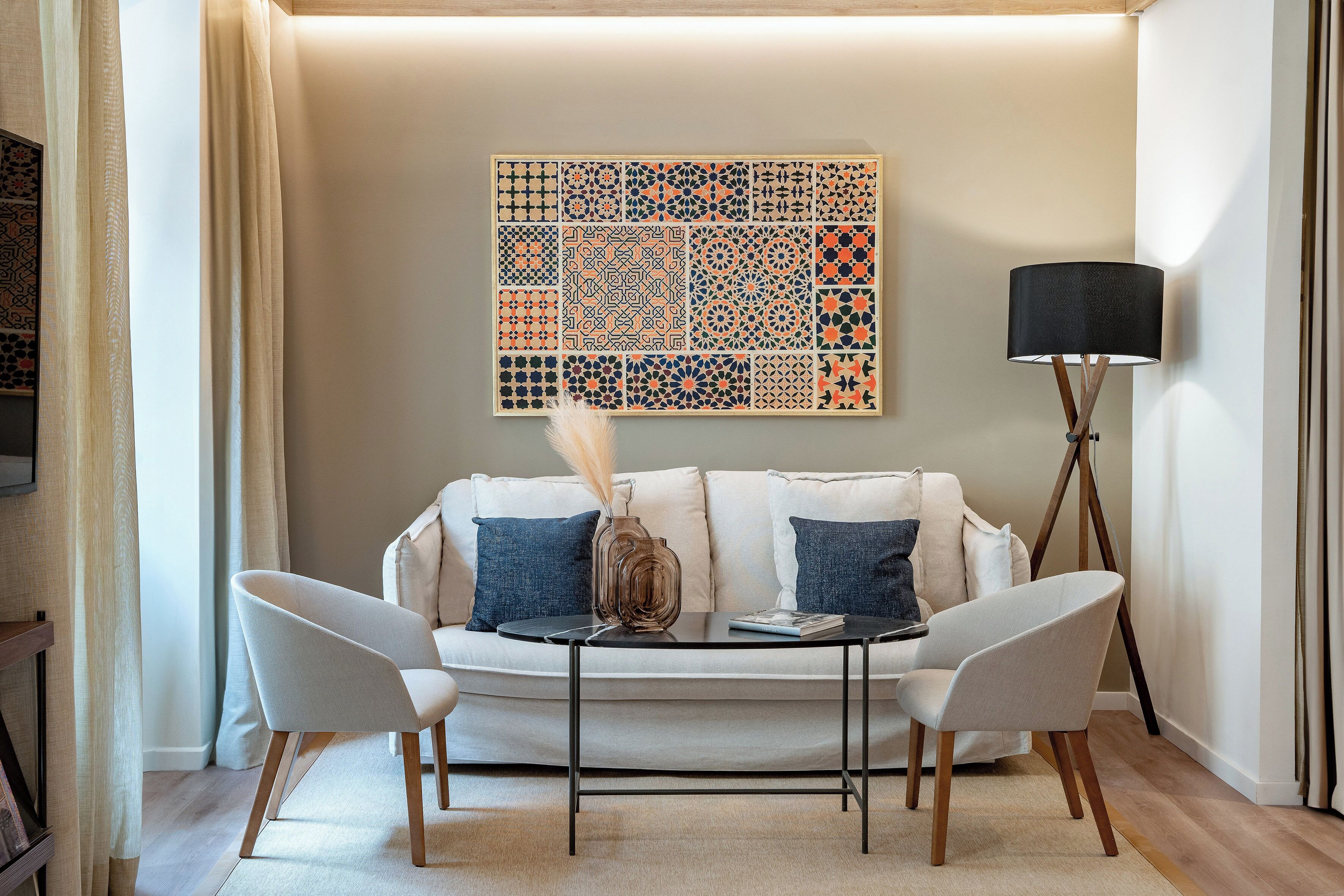 A modern living room with a white sofa, two armchairs, a coffee table, a floor lamp, and a decorative wall piece.