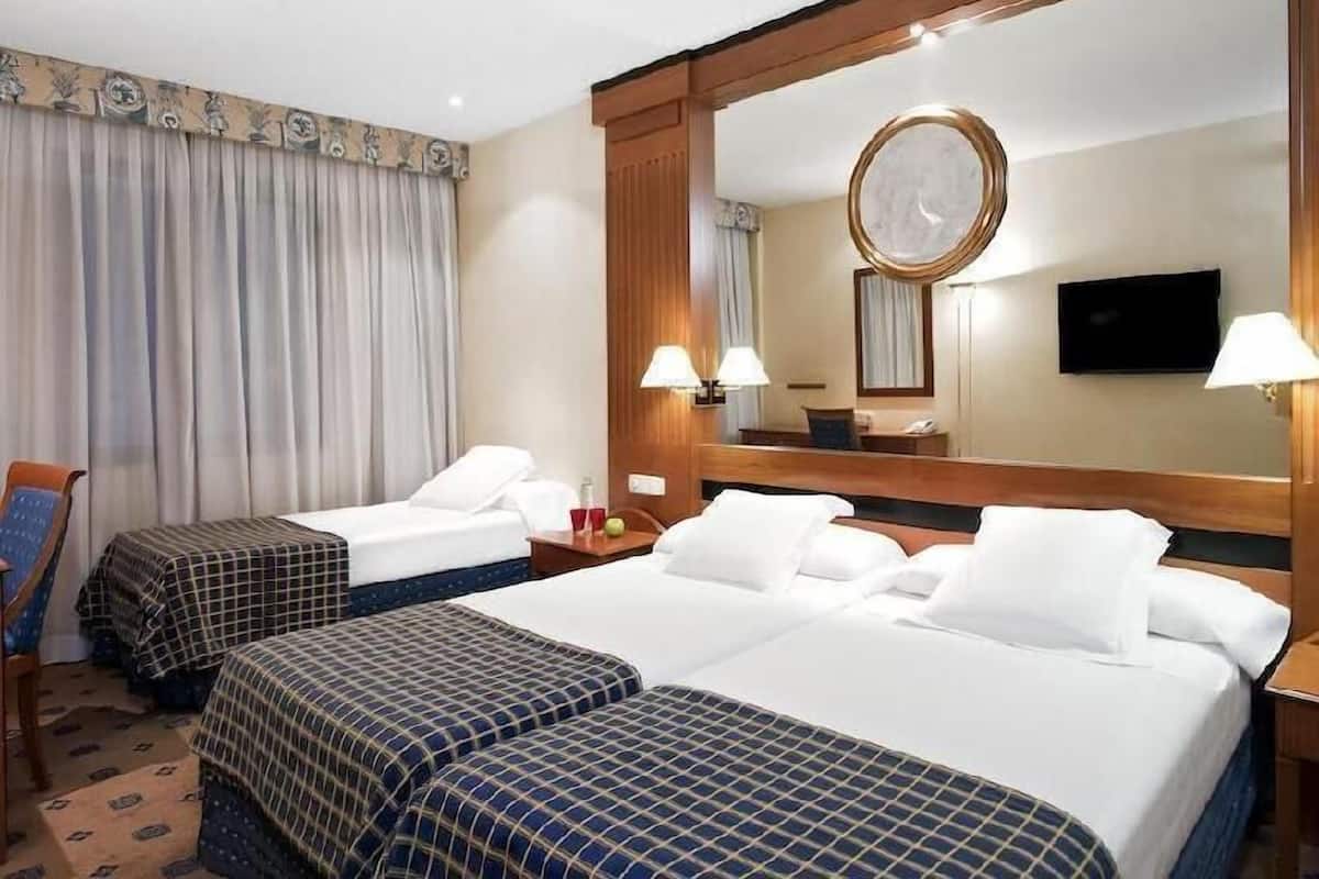 Una habitación de hotel con dos camas, un espejo grande, un televisor y un escritorio con una lámpara.