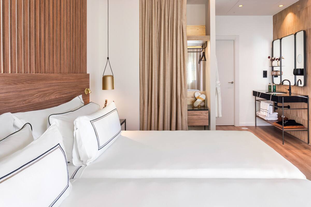 Una habitación de hotel moderna con una cama grande, paneles de madera, una tocador con espejo y una lámpara colgante.