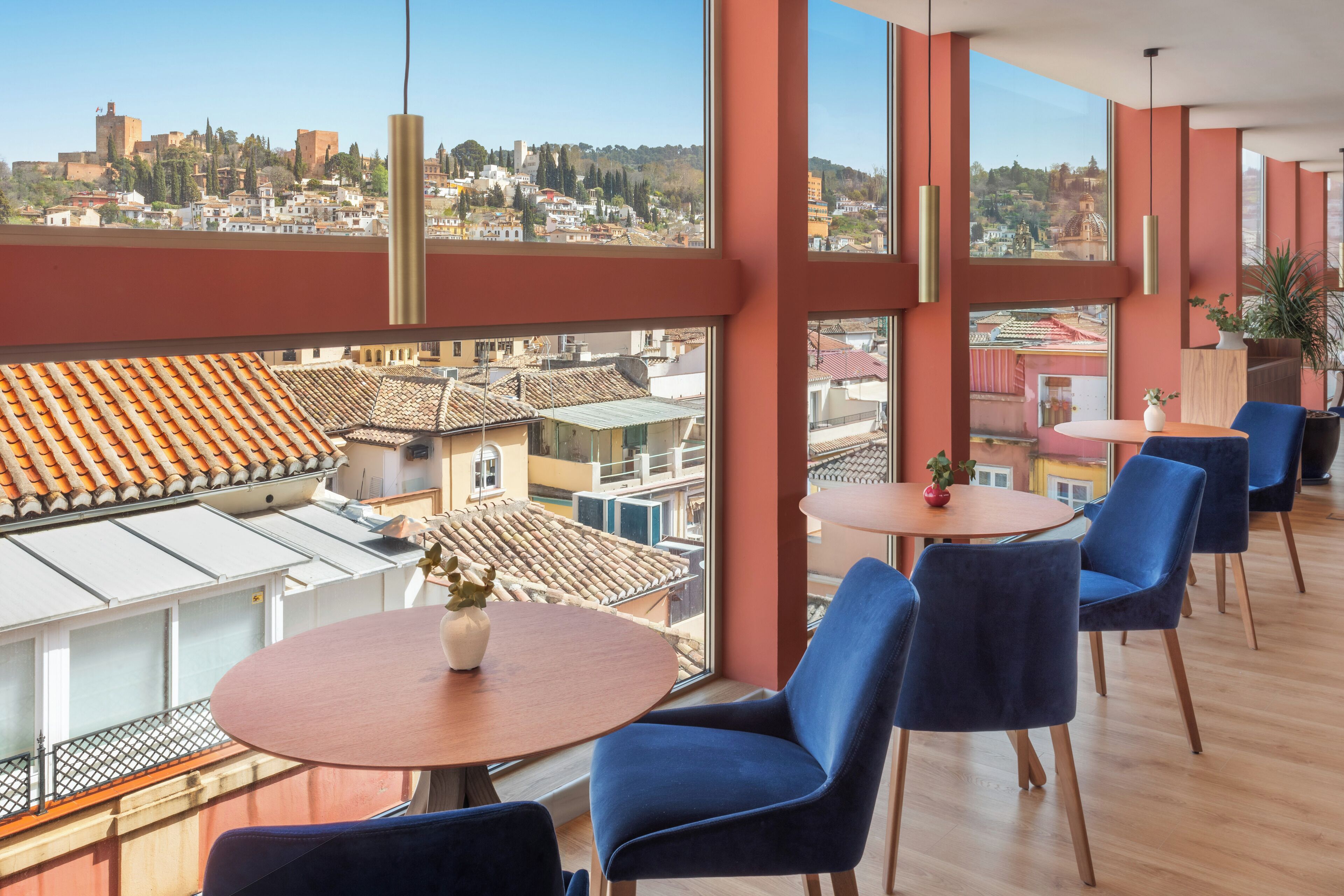 A modern interior with large windows offering a city view, a round table with chairs, and a potted plant.