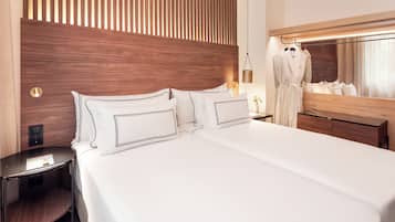 Une chambre d’hôtel moderne avec un grand lit, une tête de lit en bois, une table de chevet, un miroir et un peignoir accroché au mur.