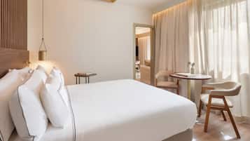 Ett hotellrum med en säng, ett sängbord, en lampa, en stol och utsikt över omgivningen genom gardiner.