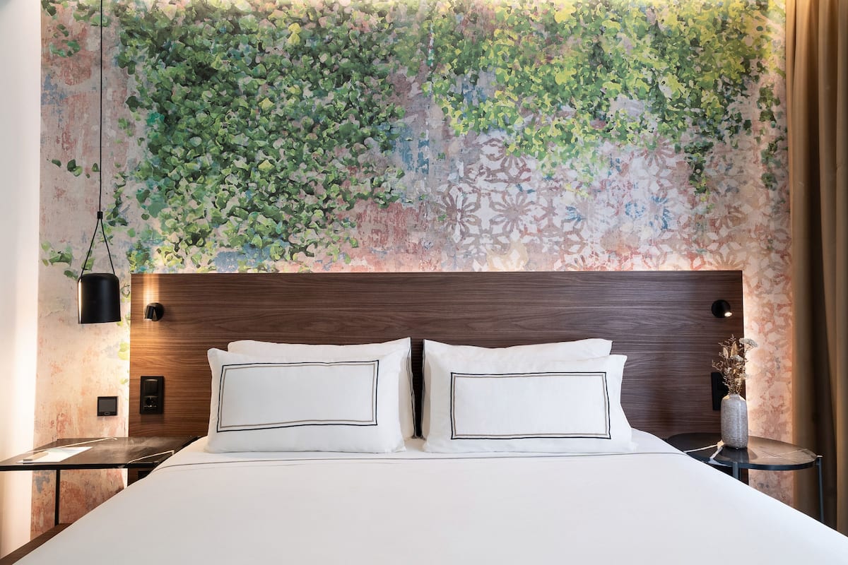 Una habitación de hotel moderna con una cama grande, cabecera de madera y un mural decorativo en la pared.