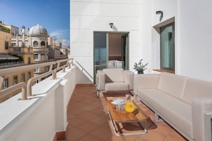 A balcony with a white sofa, a wooden coffee table, and a view of a historic building.