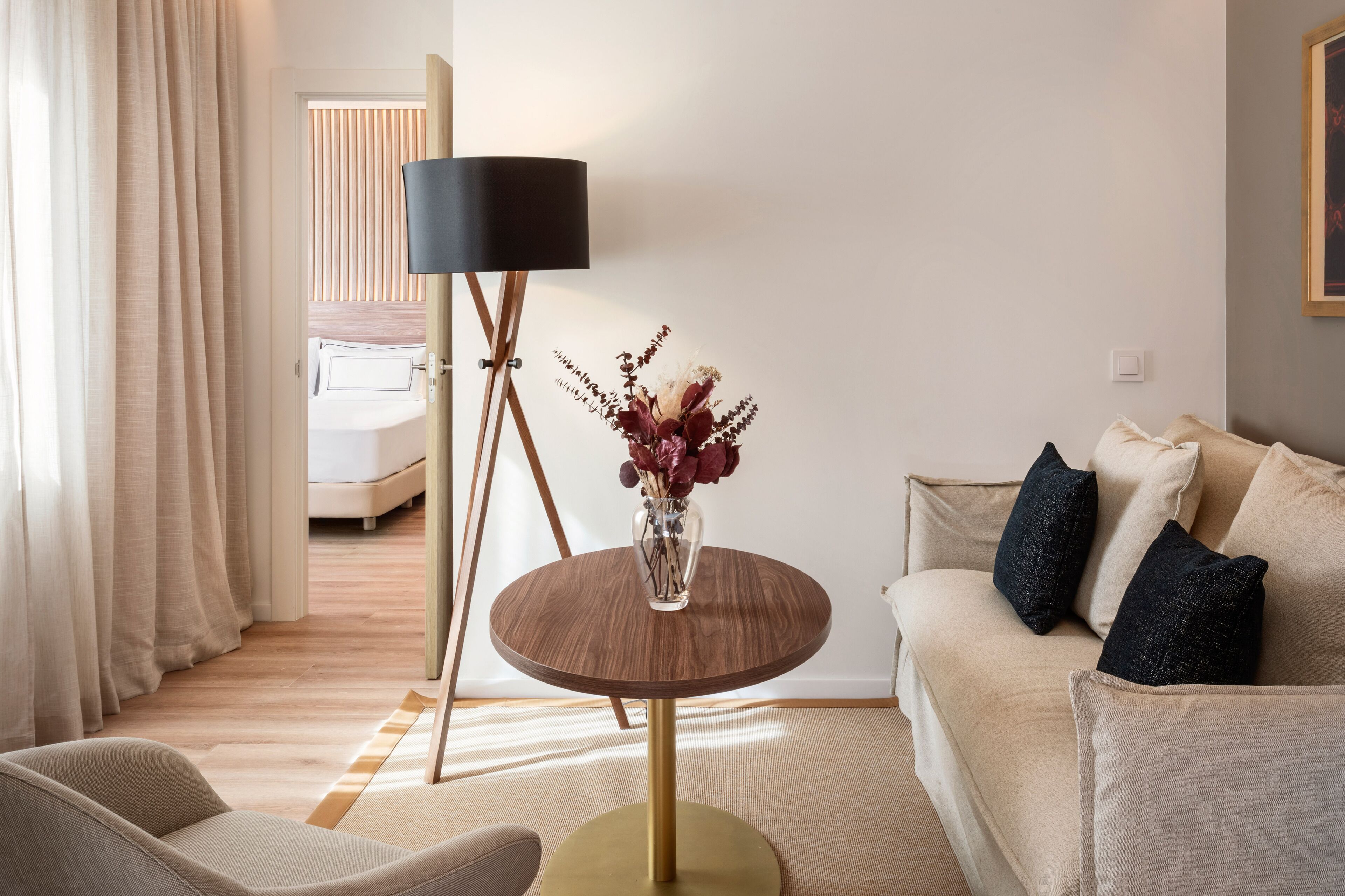 Un salon moderne avec une table ronde en bois, un lampadaire, un canapé et un lit en arrière-plan.