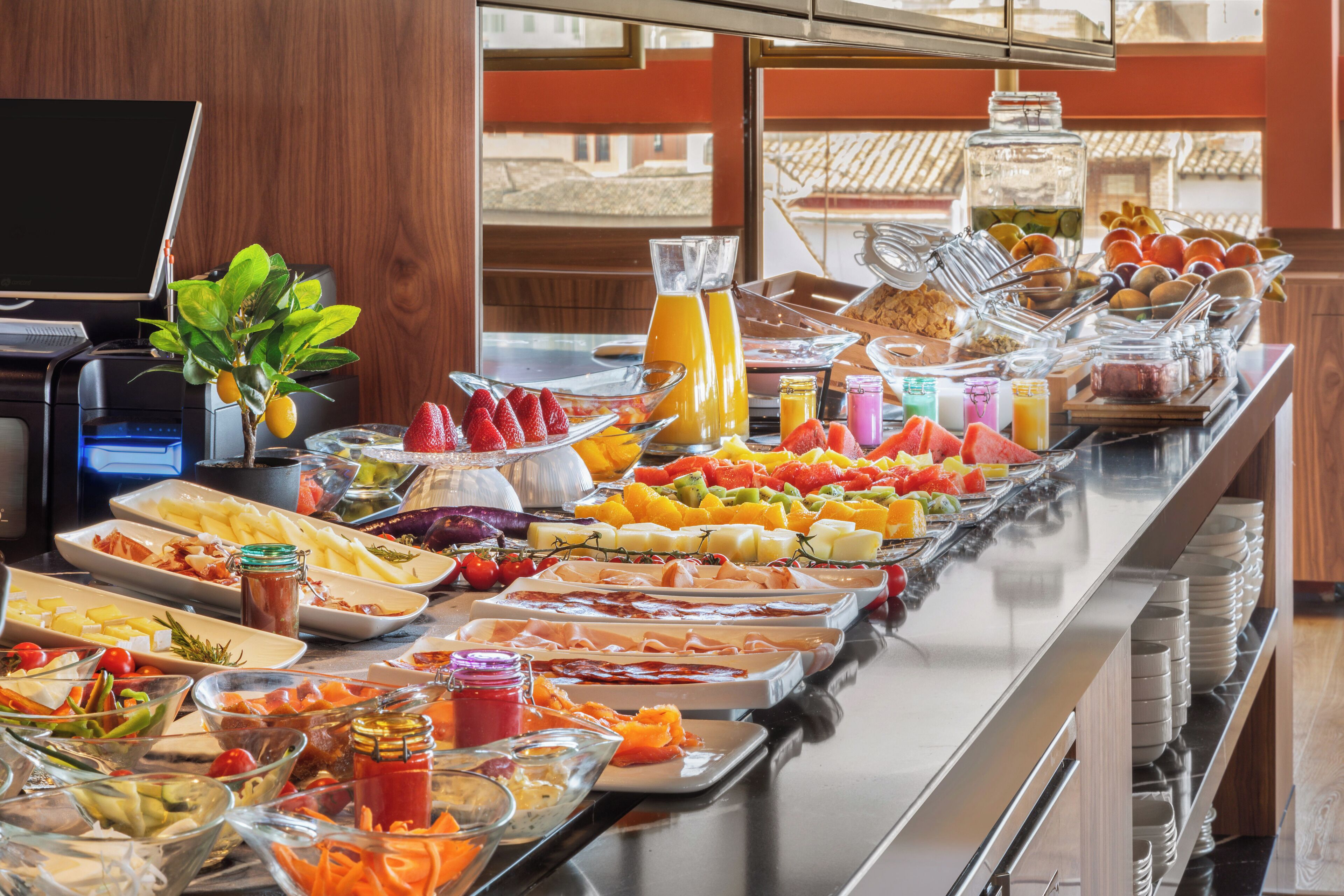 A buffet with various food items and beverages, a coffee machine, and a laptop on a table.