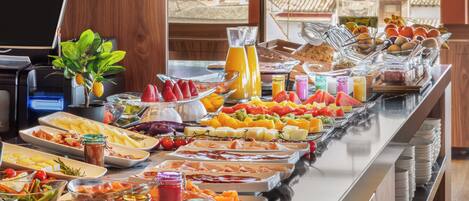 A buffet with various food items and beverages, a coffee machine, and a laptop on a table.