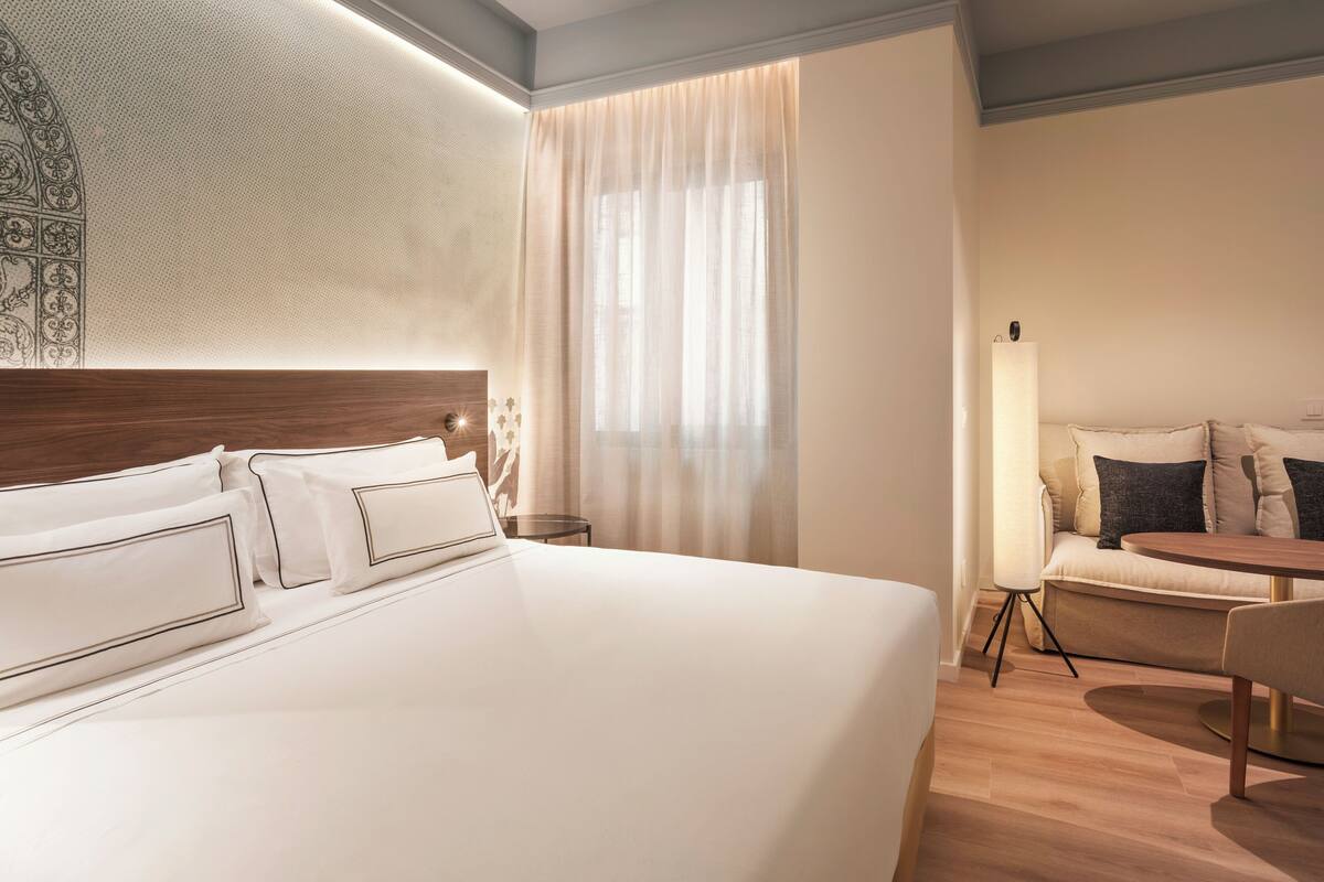 Una habitación de hotel moderna con una cama grande, una mesita de noche, una lámpara, un sofá y una pequeña mesa.