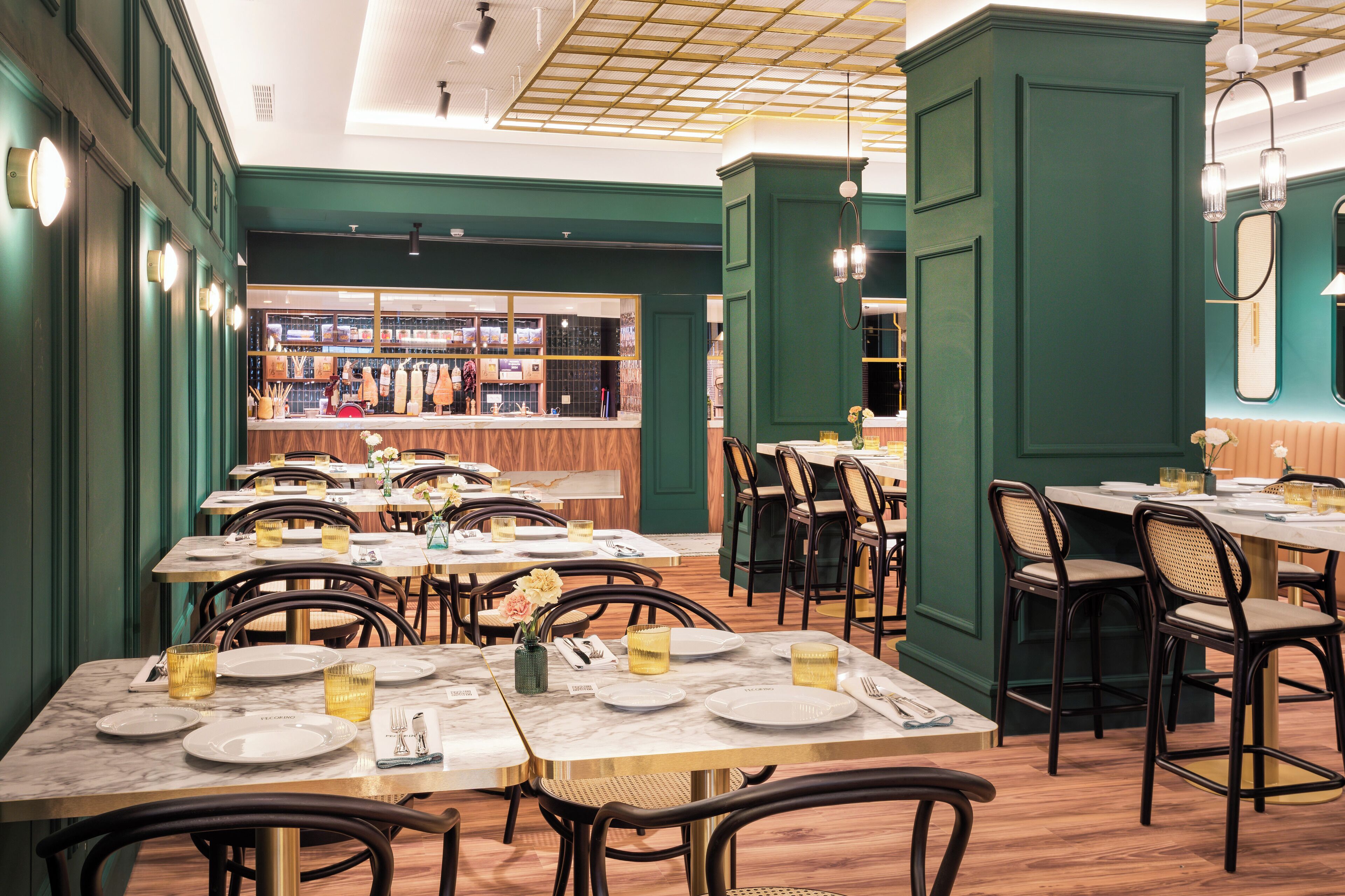 L’intérieur d’un restaurant, avec de nombreuses tables et chaises, un bar à l’arrière-plan et des murs verts.