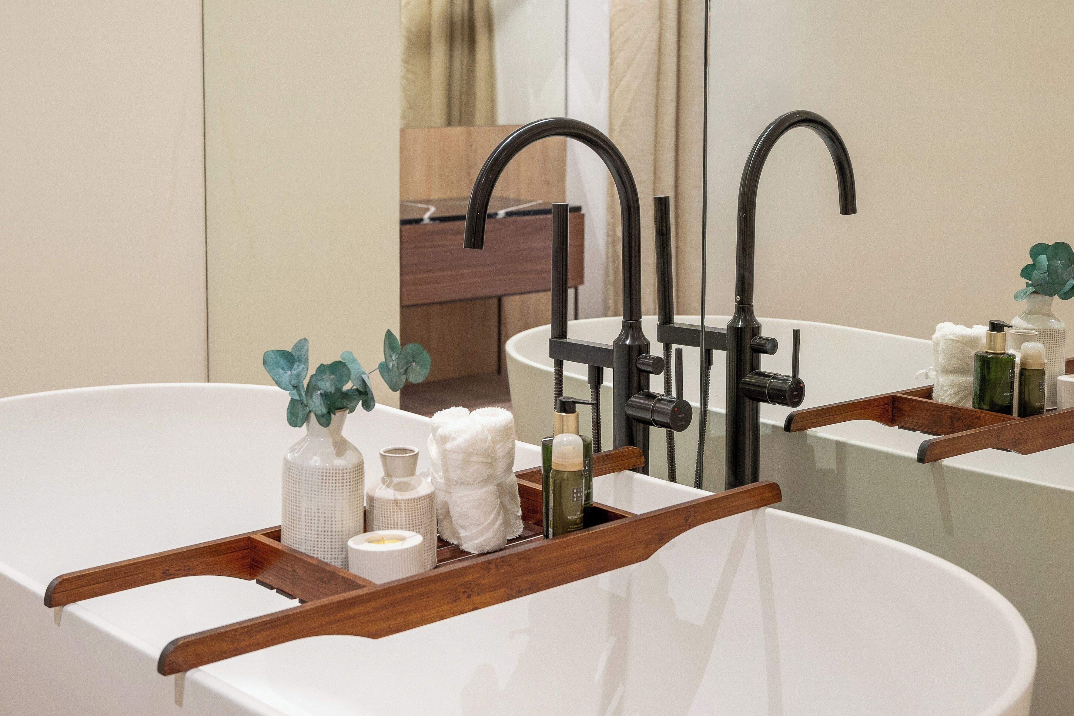 Une salle de bain moderne avec une baignoire sur pieds, un plateau en bois contenant des articles de toilette et un meuble-lavabo en bois.